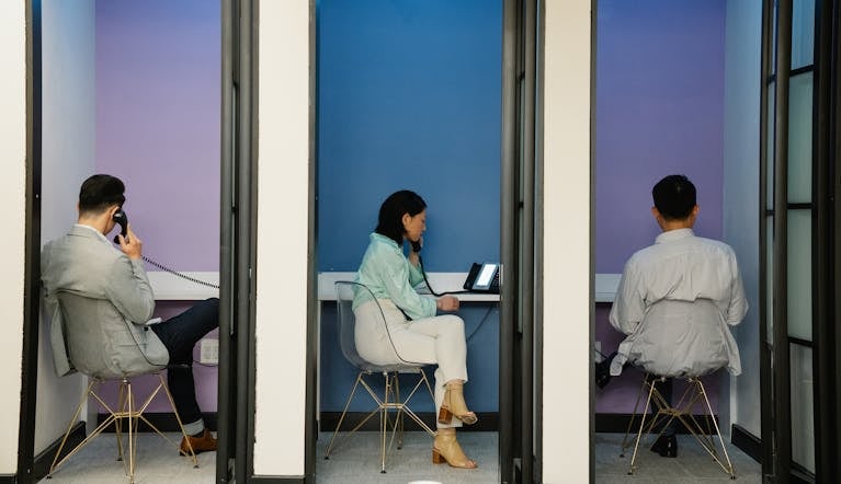 Business professionals using phone booths for communication in a modern office space.