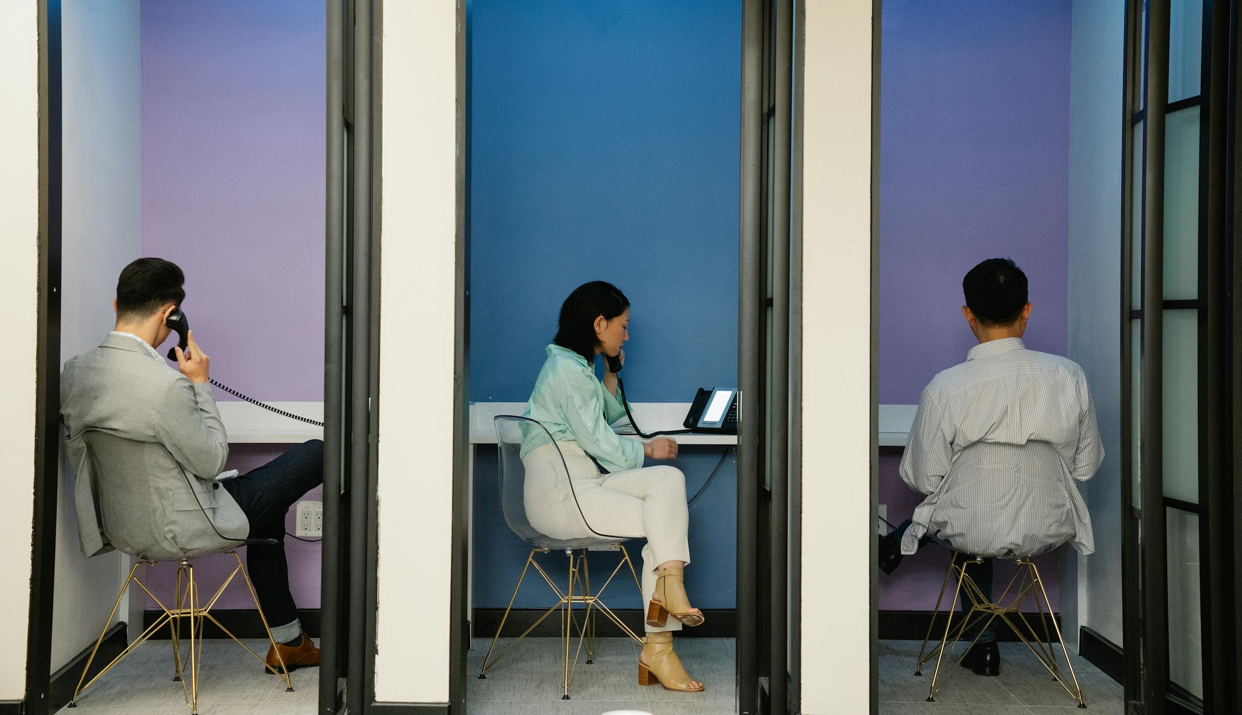 Business professionals using phone booths for communication in a modern office space.