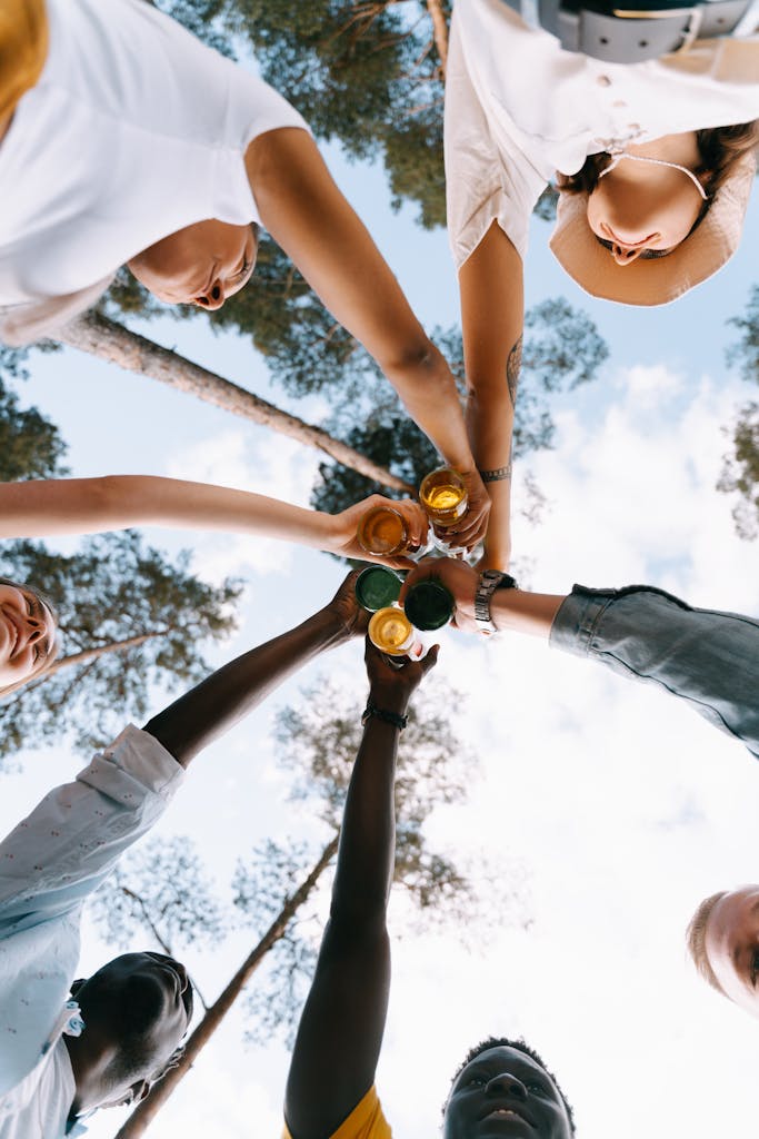 A diverse group of friends clinking glasses under pine trees, celebrating outdoors.